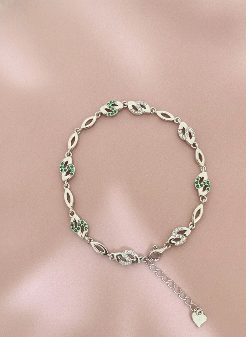 Silver bracelet with green gemstones on a pink background