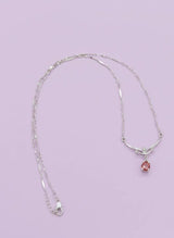 Silver necklace with a pink pendant on a light purple background