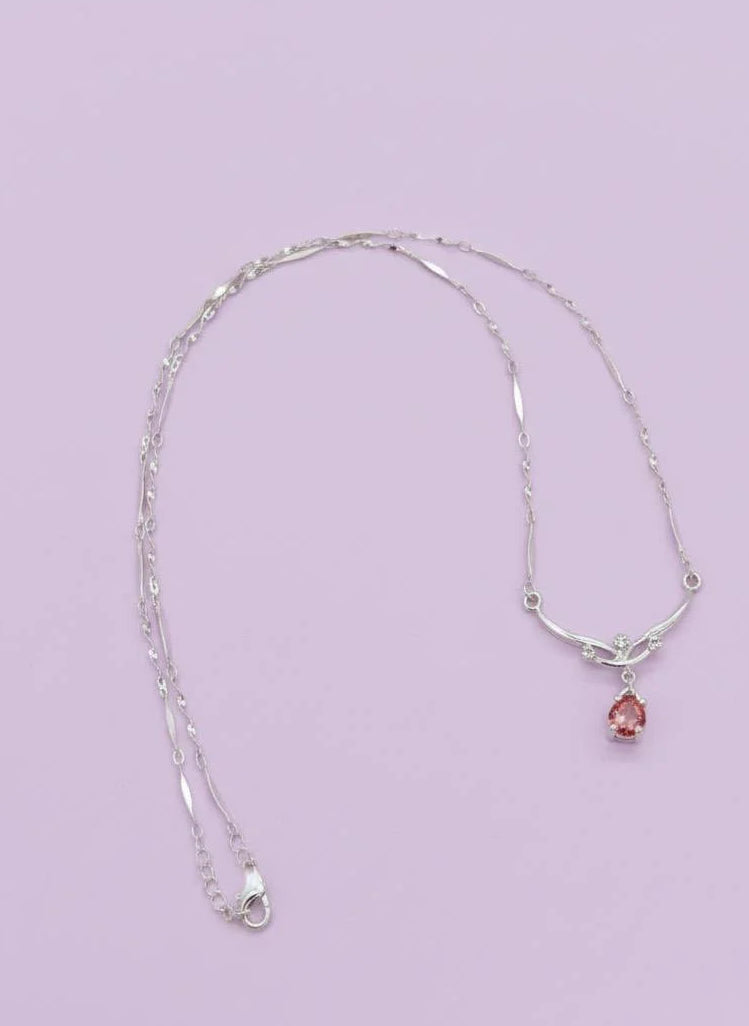Silver necklace with a pink pendant on a light purple background