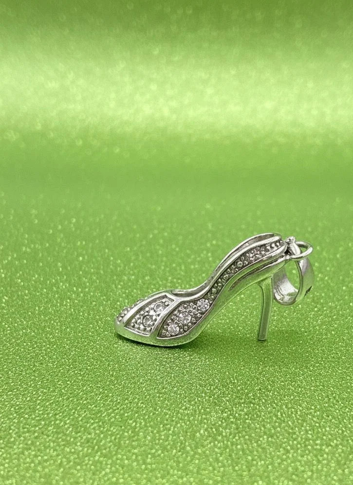 Silver high-heeled shoe charm on a green textured background