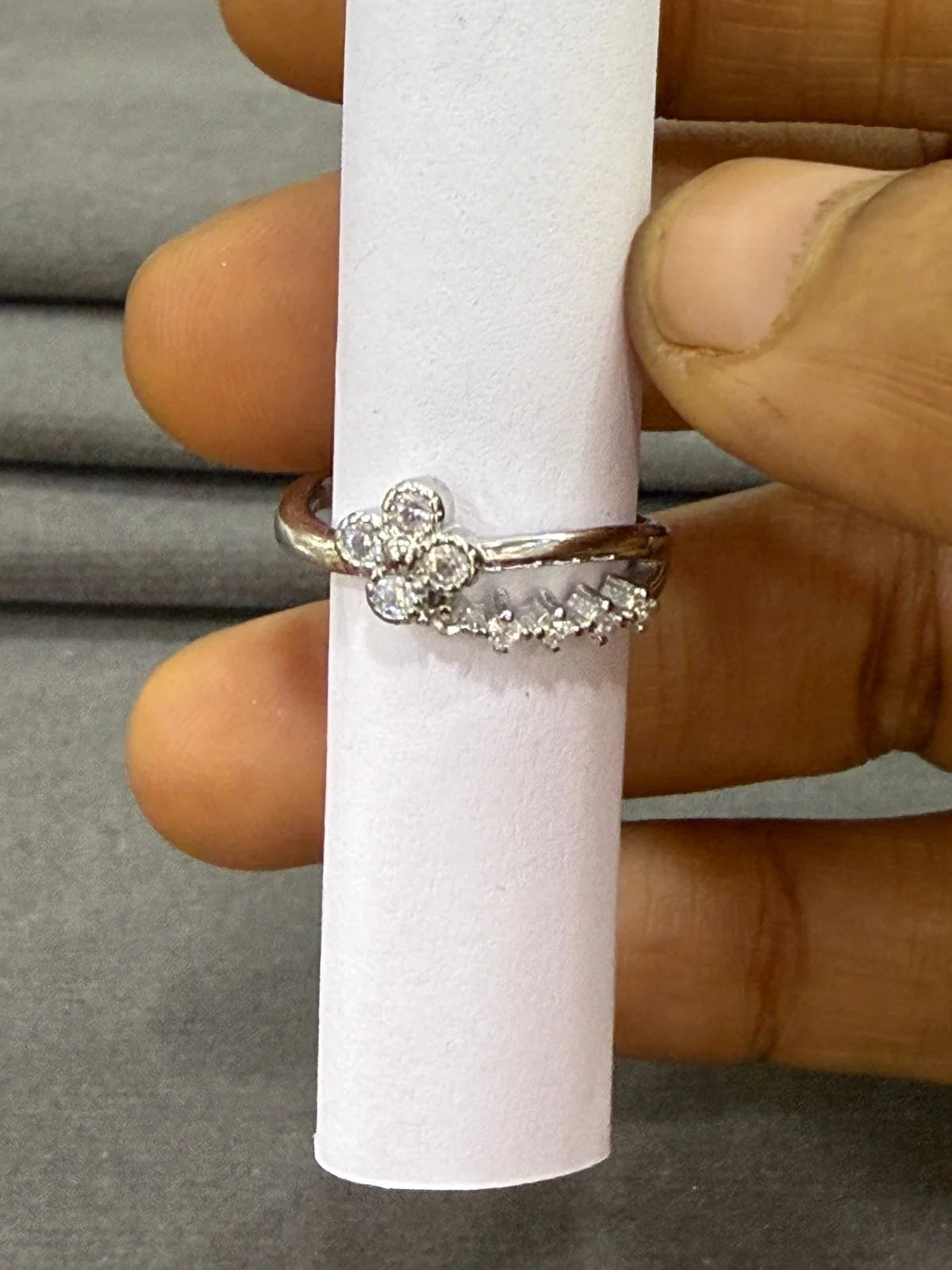 Silver ring with floral design on a white cylindrical stand, held by a hand.