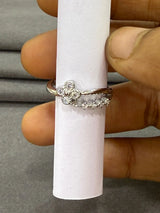 Silver ring with floral design on a white cylindrical stand, held by a hand.