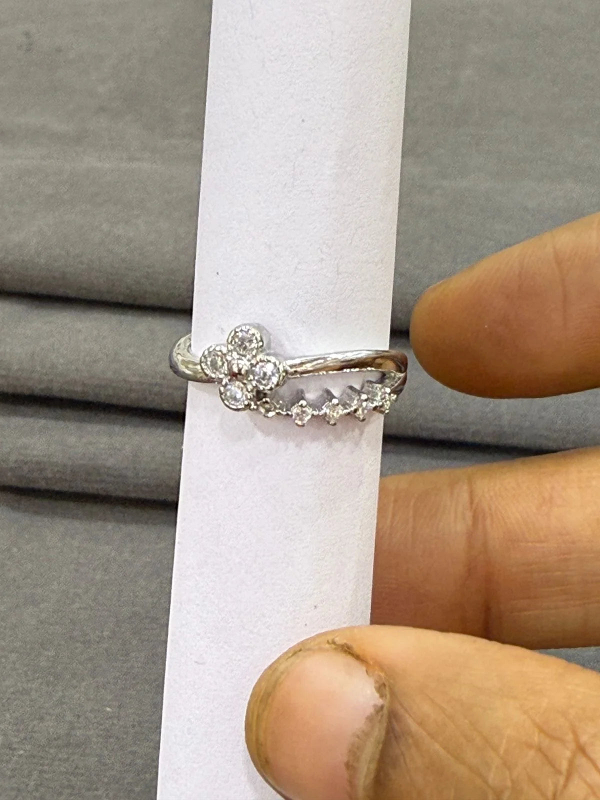 Silver ring with small diamonds held by a hand on a gray background