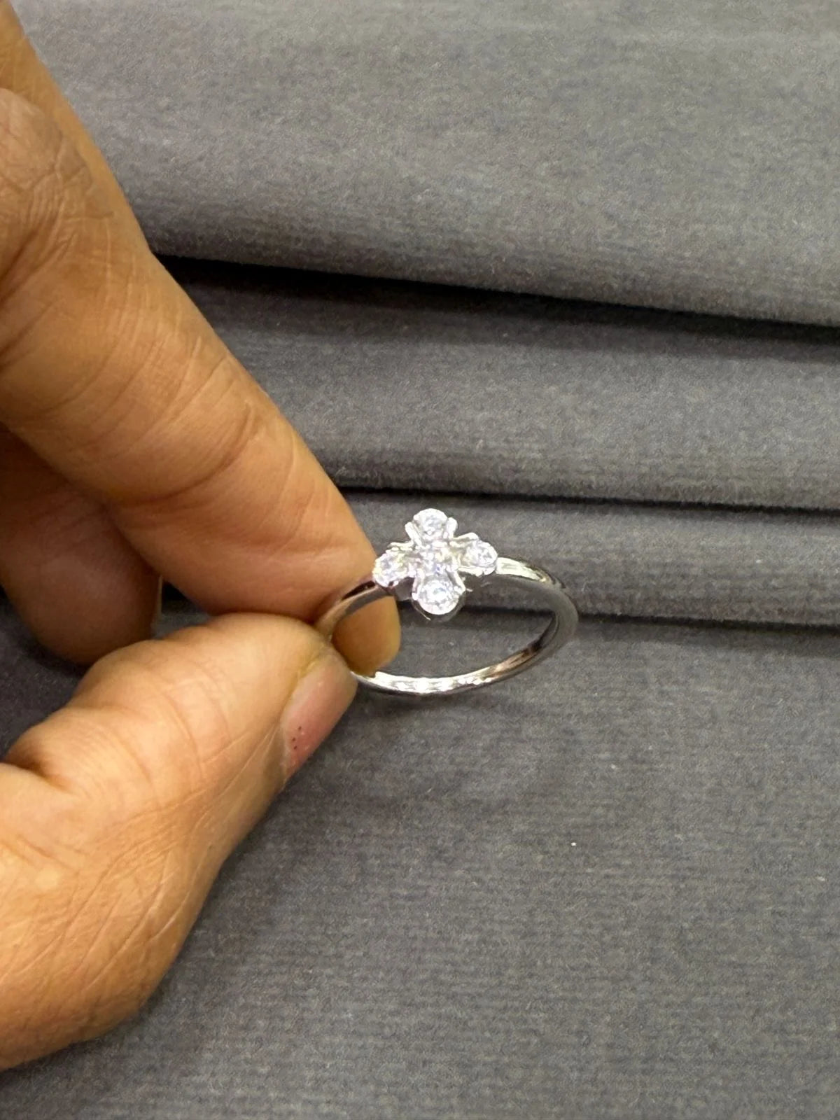Silver ring with clover held by a hand on a gray fabric background