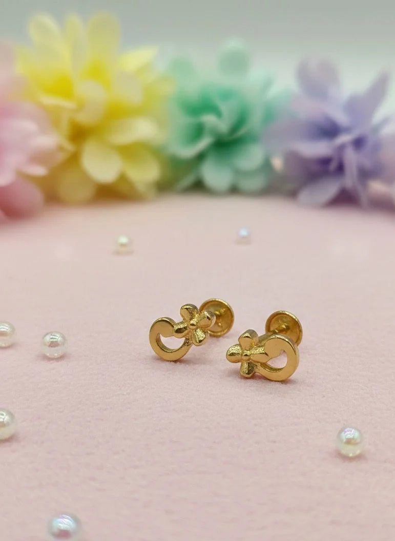 Gold earrings on a pink surface with scattered pearls and pastel flowers in the background