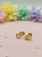 Gold earrings on a pink surface with scattered pearls and pastel flowers in the background