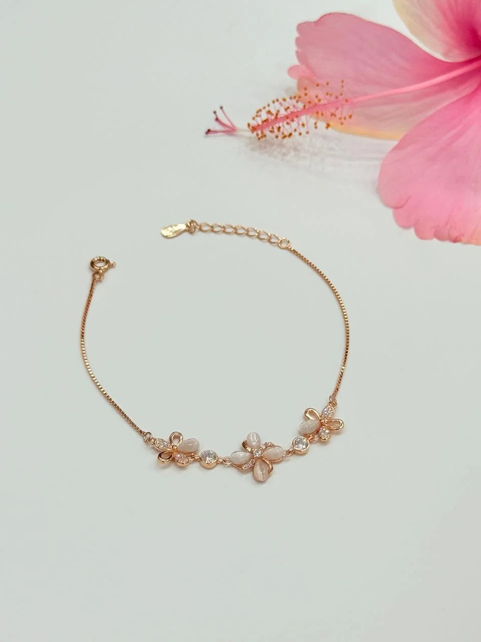 Rose gold bracelet with floral elements on a light gray background with a pink flower.