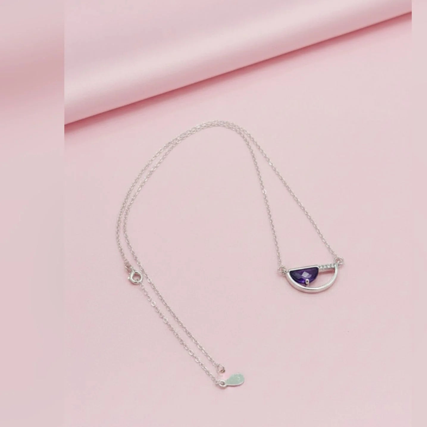 Silver necklace with a purple pendant on a pink fabric background