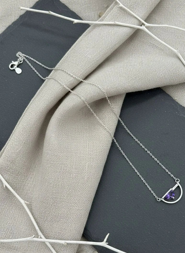 Silver necklace with a purple gemstone pendant on a textured fabric background