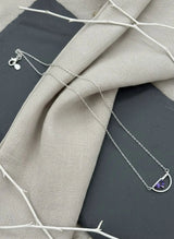 Silver necklace with a purple gemstone pendant on a textured fabric background