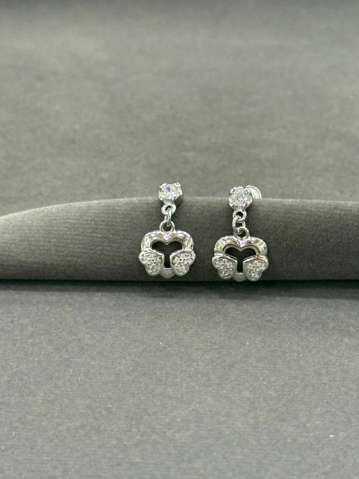 Pair of silver earrings with heart-shaped designs on a gray surface