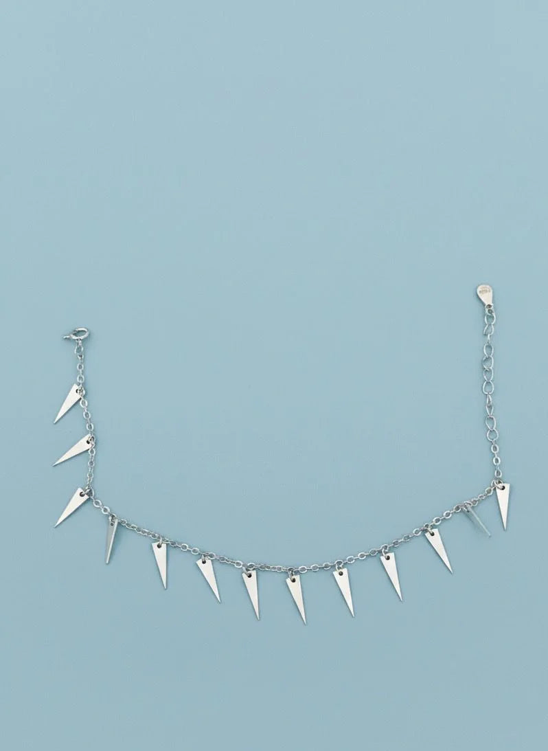 Silver bracelet with spike-like hangings on a light blue background