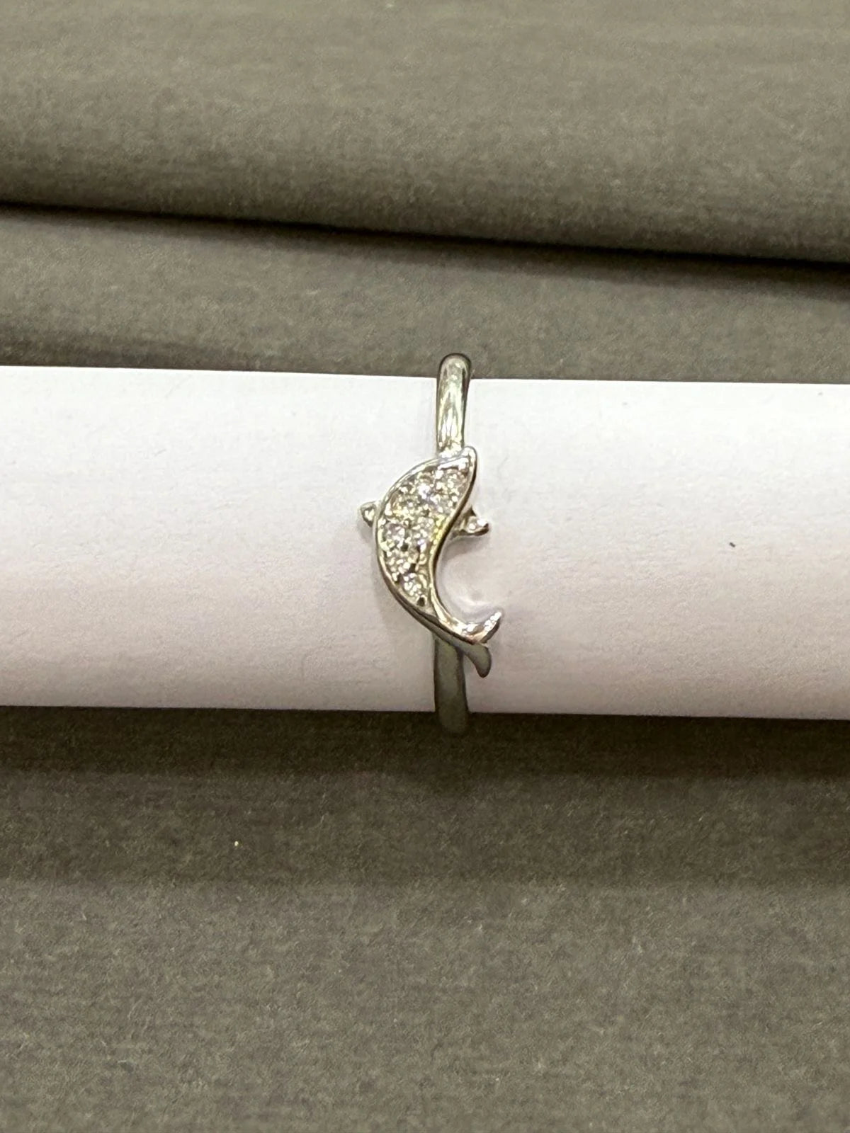 Silver ring with a dolphin design on a white cylindrical object against a gray background