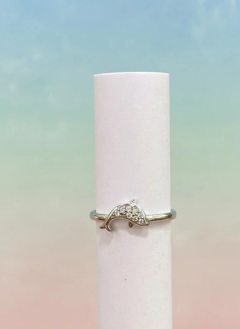 Dolphin-shaped ring on a white cylindrical object with a pastel gradient background