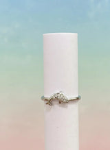 Dolphin-shaped ring on a white cylindrical object with a pastel gradient background