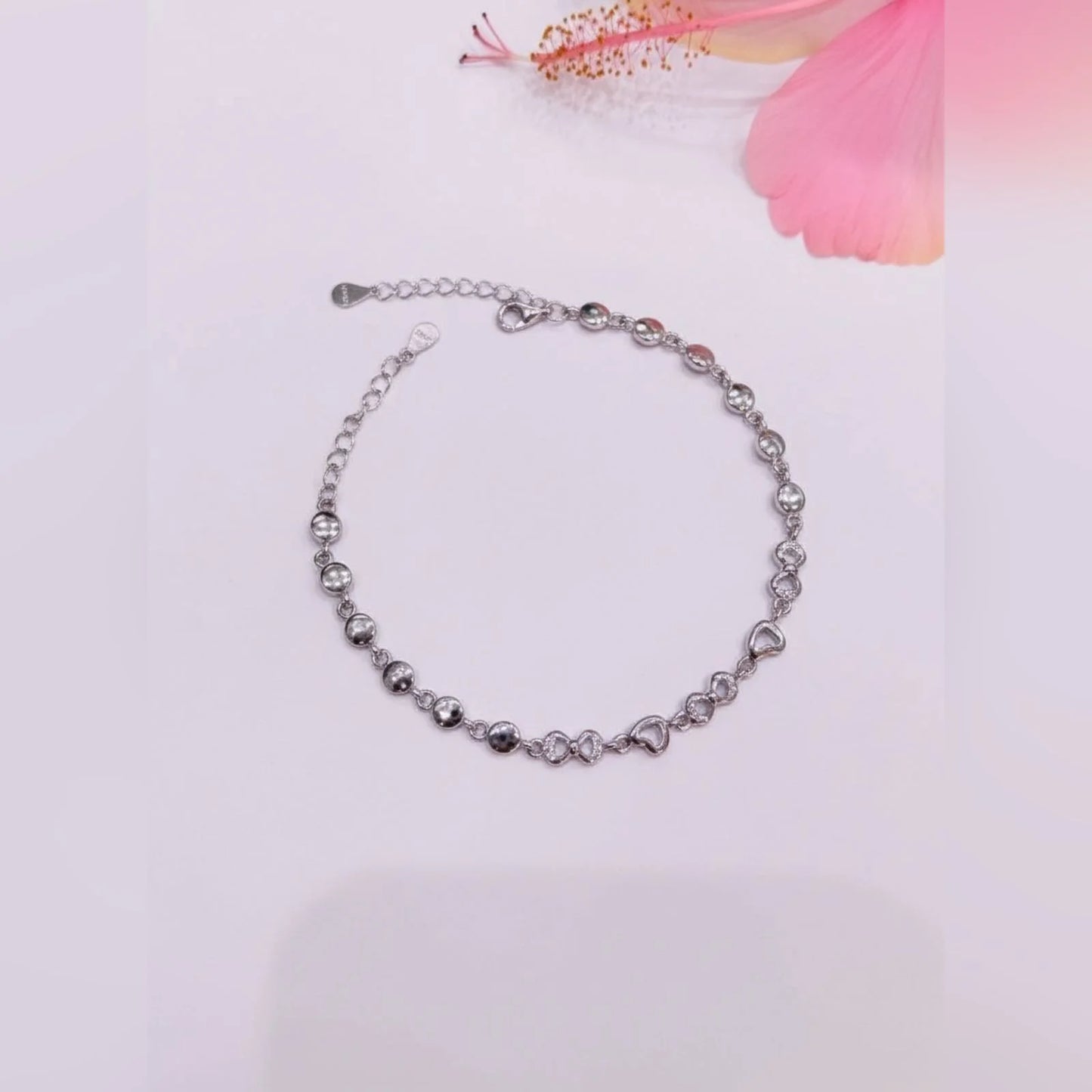 Silver bracelet with heart-shaped beads on a light pink background