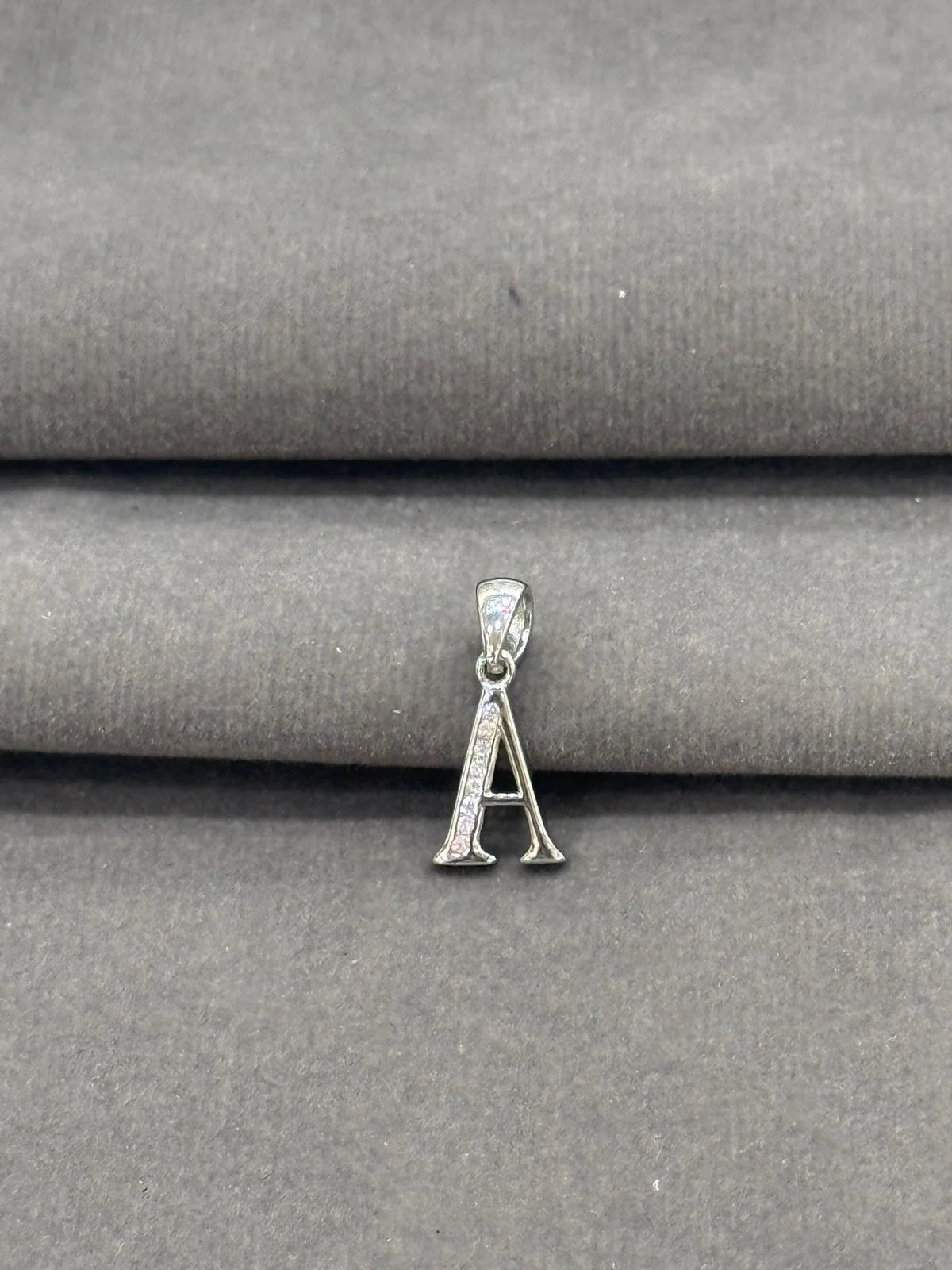Silver pendant with letter 'A' on a gray fabric background