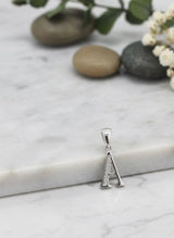 Silver pendant with letter 'A' on a marble surface with stones and flowers.