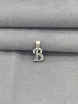 Silver 'B' pendant on a gray fabric background