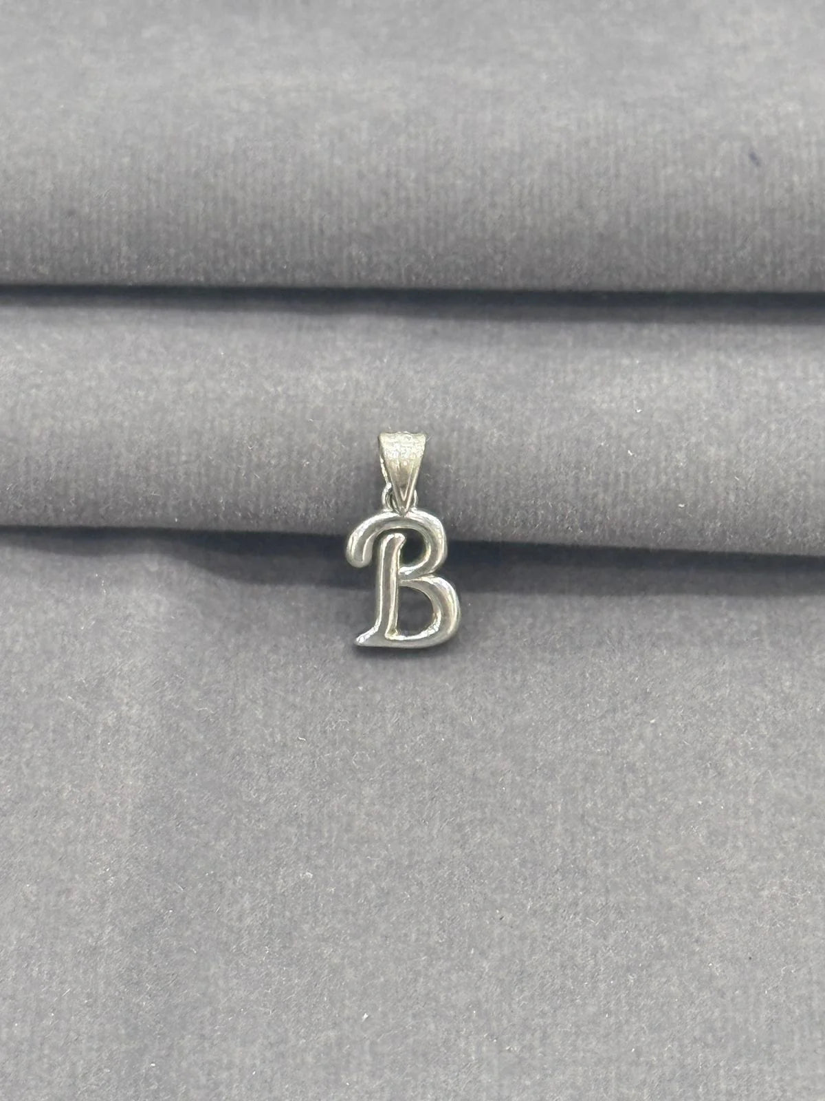 Silver 'B' pendant on a gray fabric background