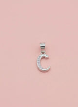 Silver C pendant with embedded stones on a pink background