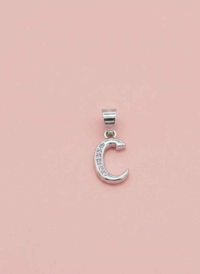 Silver C pendant with embedded stones on a pink background