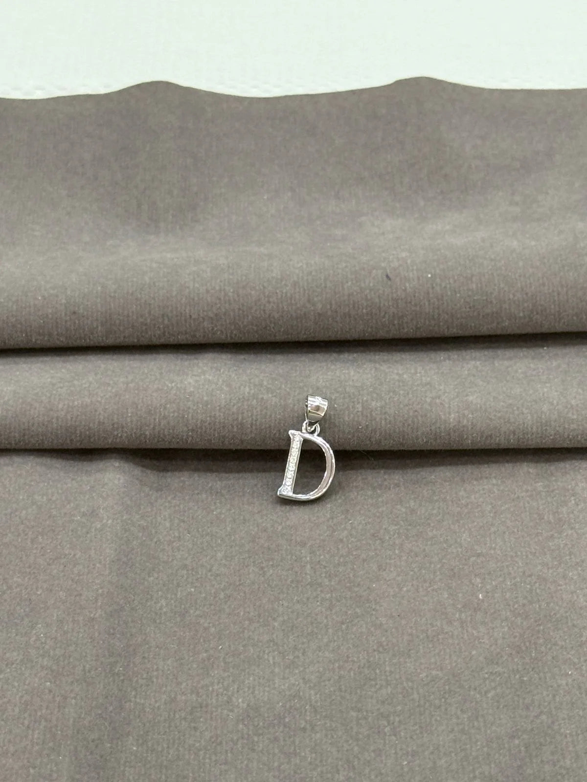 Silver 'D' pendant on a gray fabric background