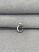 Silver G charm on a gray fabric background