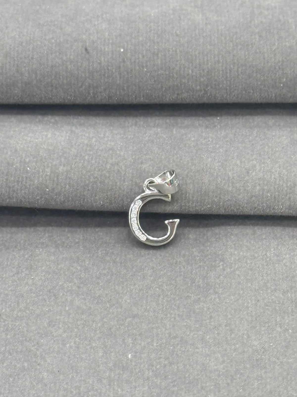 Silver G charm on a gray fabric background