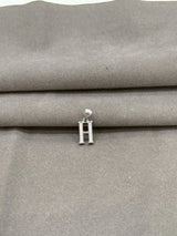 Silver 'H' pendant on a gray fabric background