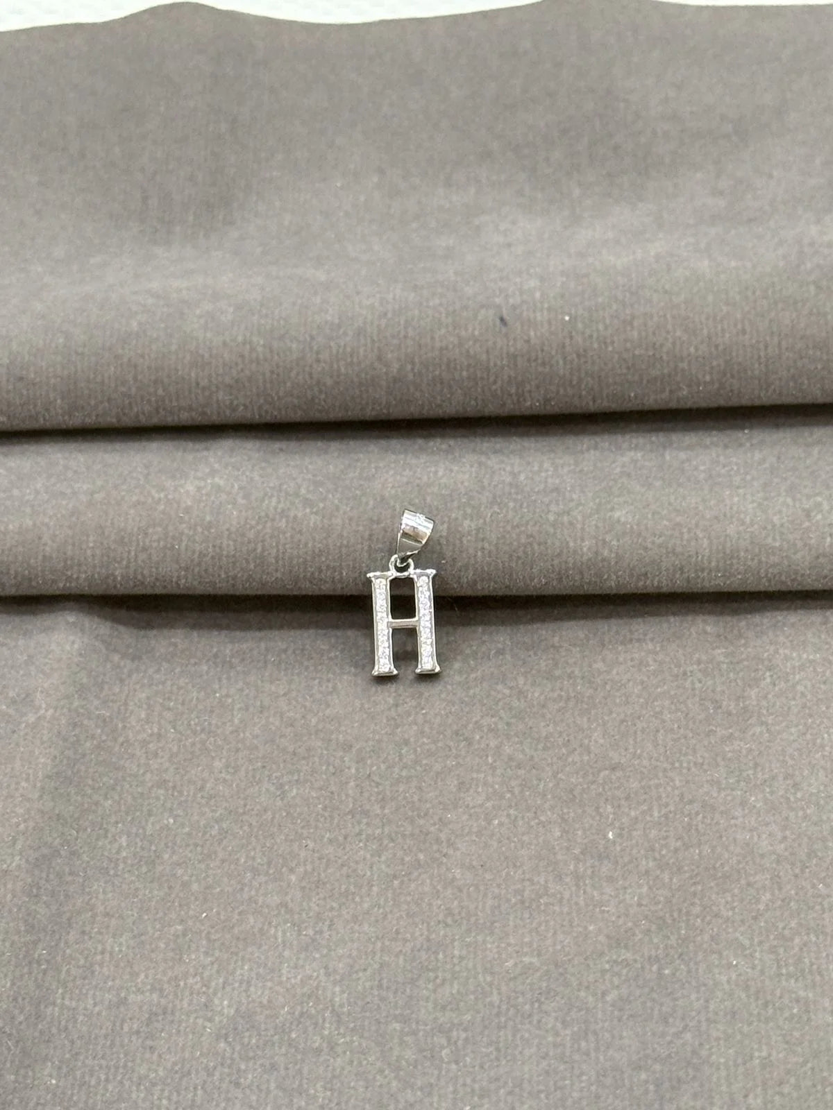 Silver 'H' pendant on a gray fabric background