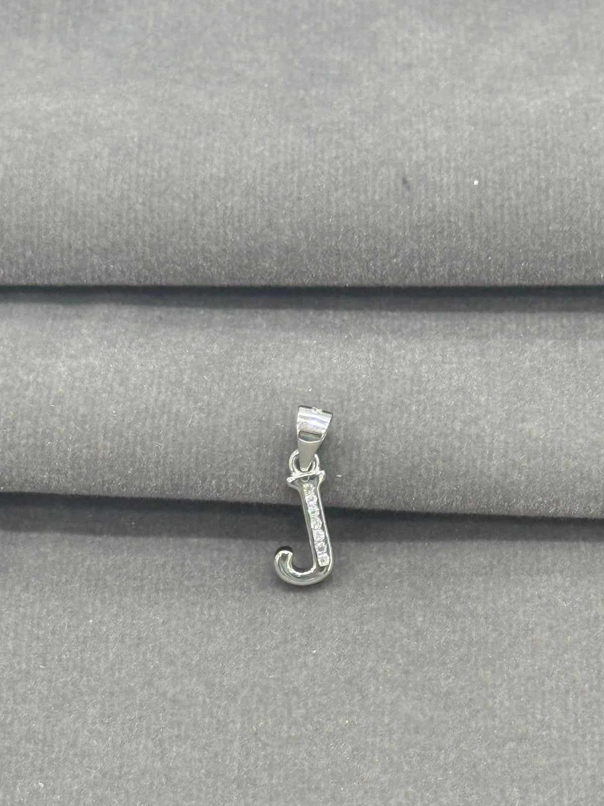 Silver letter 'J' pendant on a gray fabric background