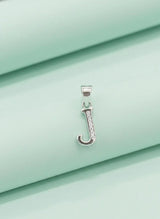 Silver pendant with a letter 'J' on a light green fabric background