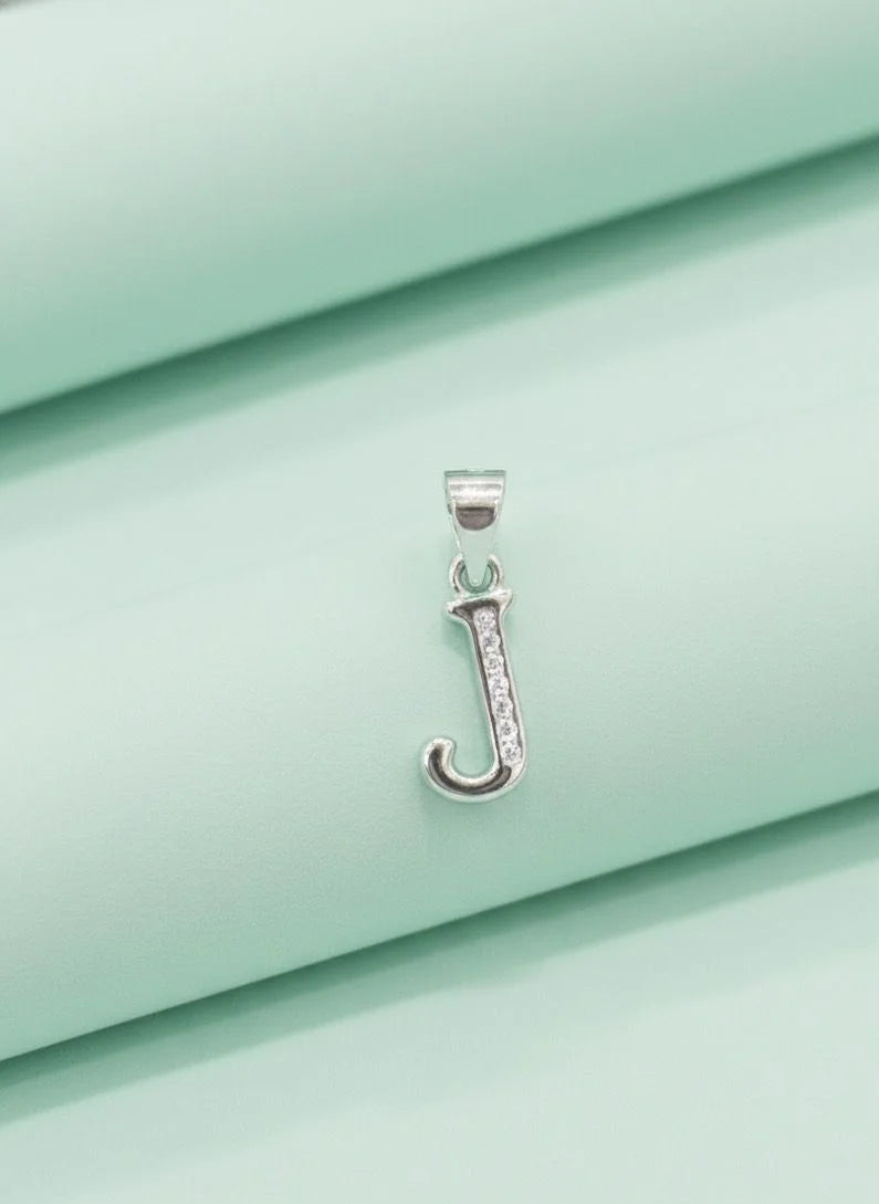 Silver pendant with a letter 'J' on a light green fabric background