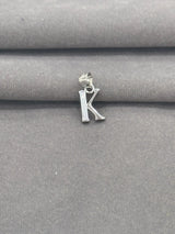 Silver 'K' pendant on a gray fabric background