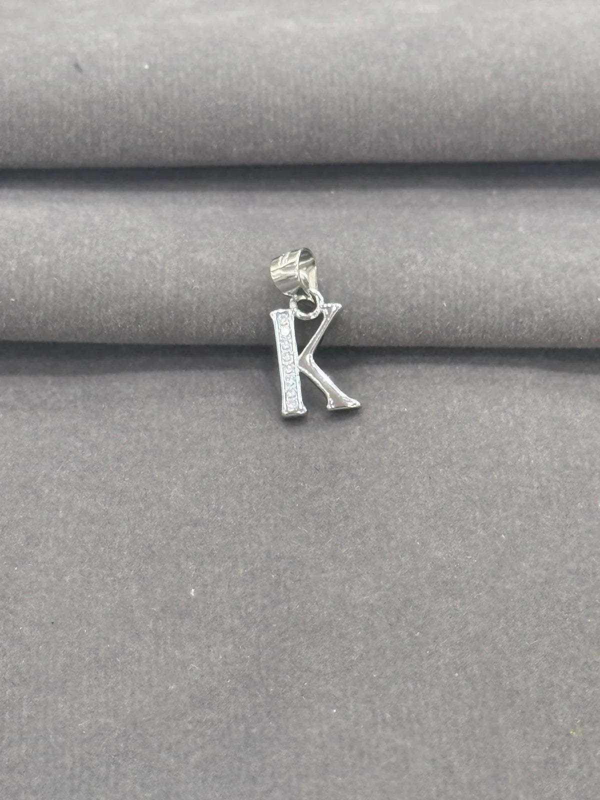 Silver 'K' pendant on a gray fabric background