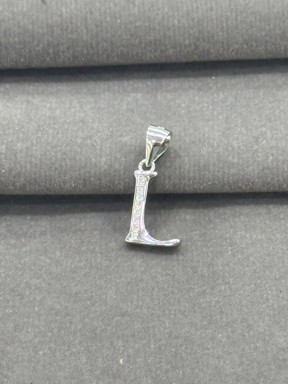 Silver 'L' pendant on a gray fabric background