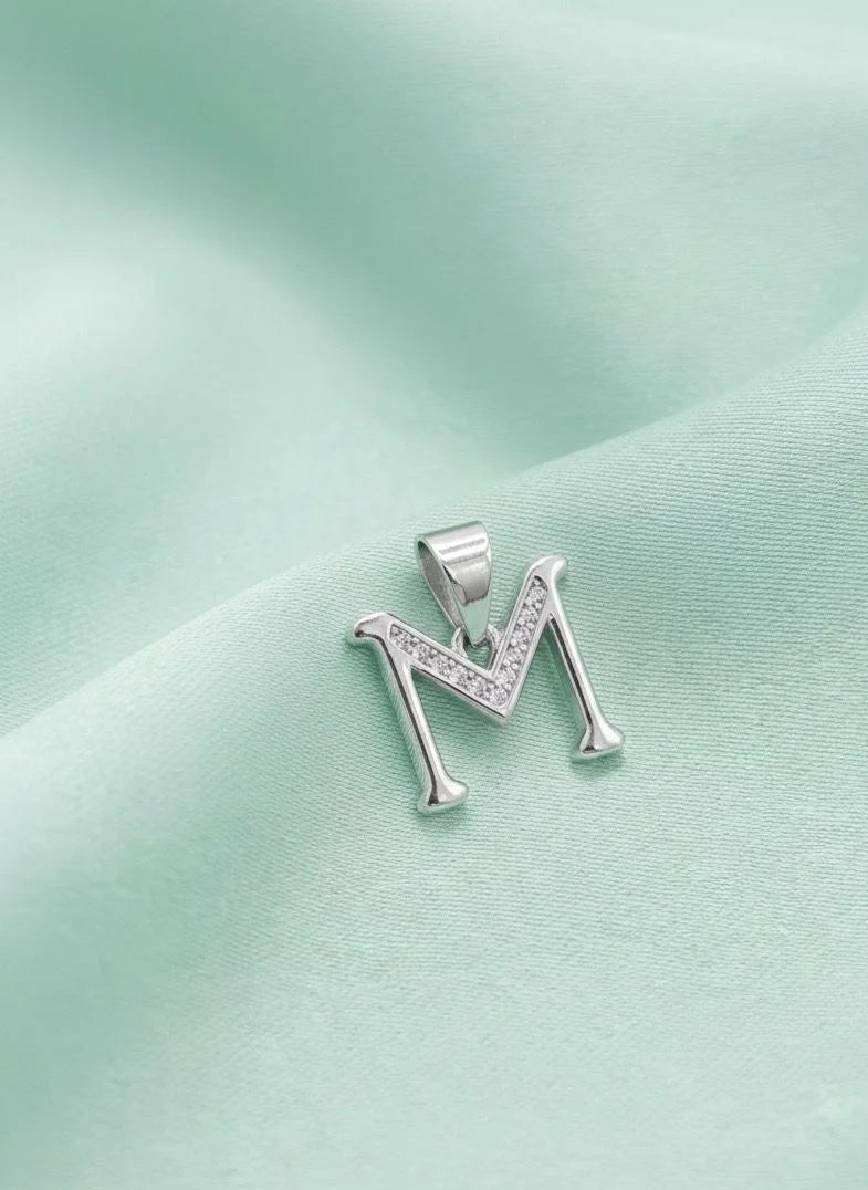 Silver 'M' pendant on a light green fabric background