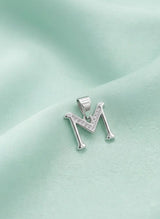 Silver 'M' pendant on a light green fabric background