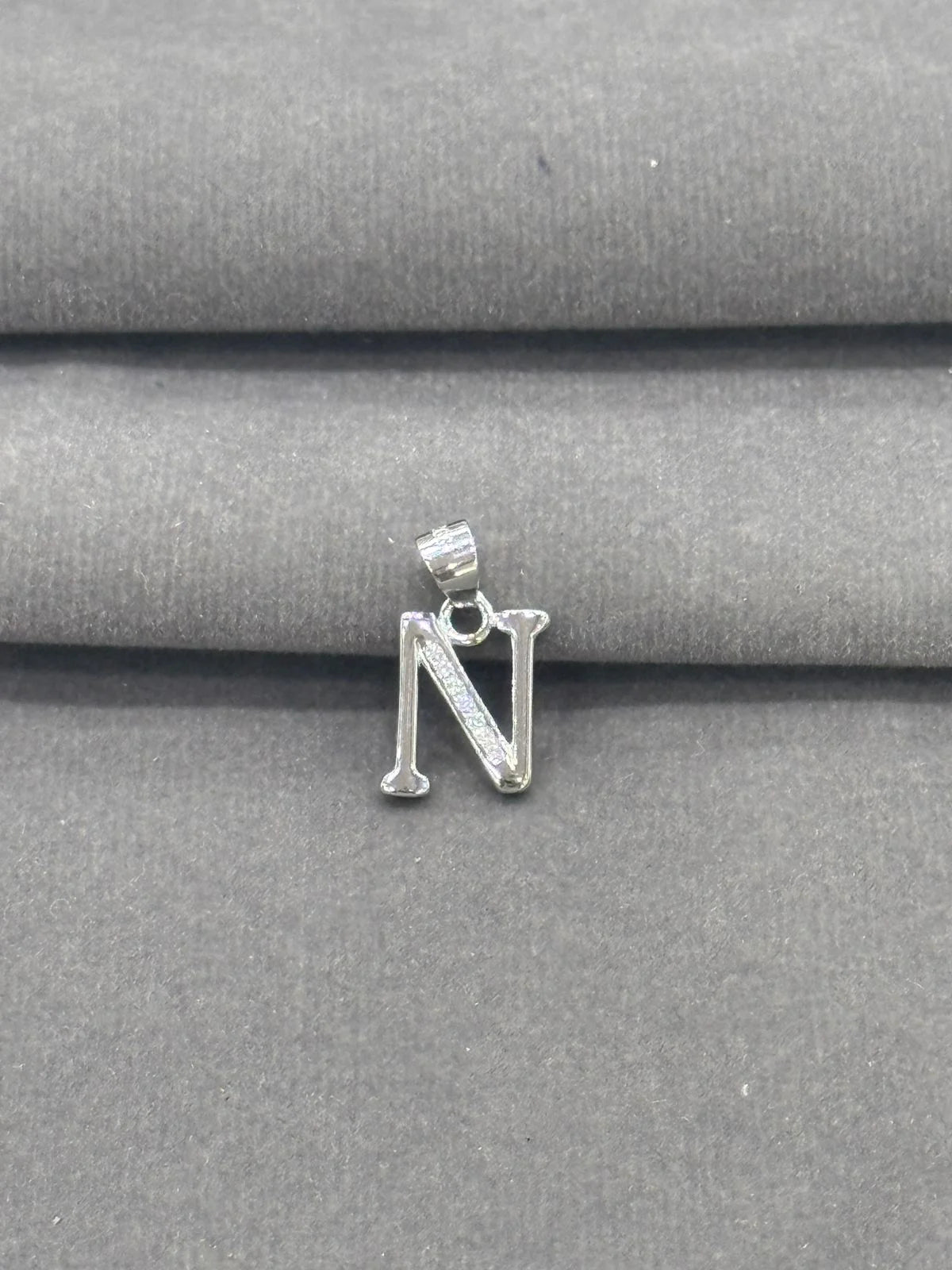Silver letter 'N' pendant on a gray fabric background