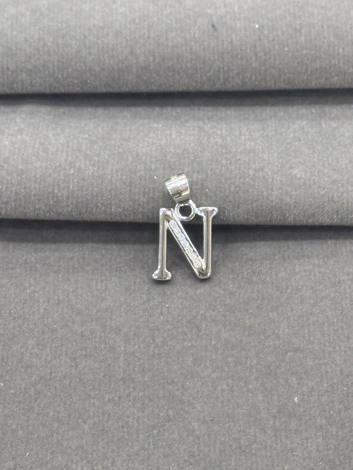 Silver letter 'N' pendant on a gray fabric background