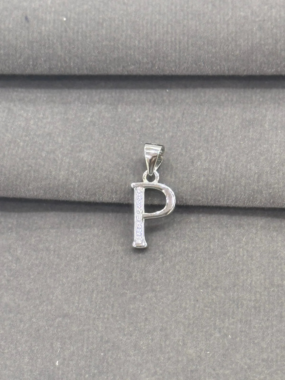 Silver 'P' pendant on a gray fabric background