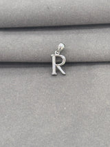 Silver 'R' pendant on a gray fabric background