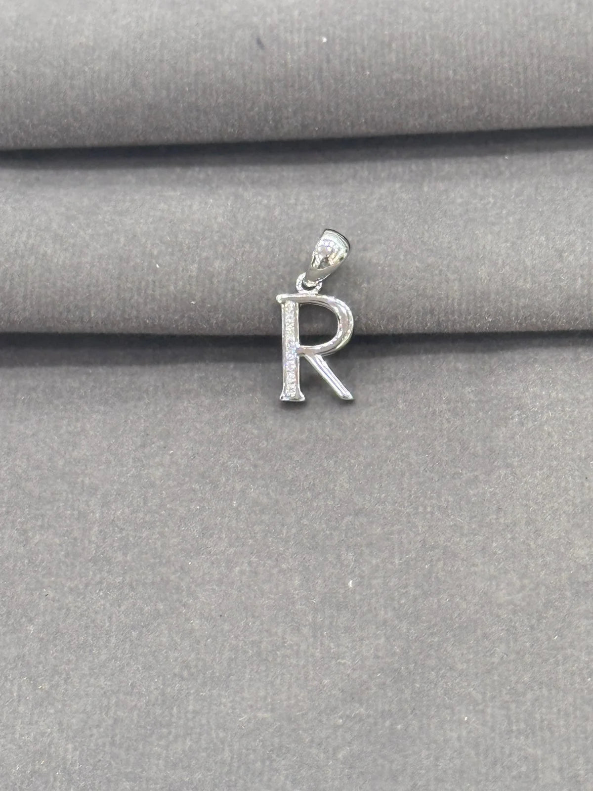 Silver 'R' pendant on a gray fabric background