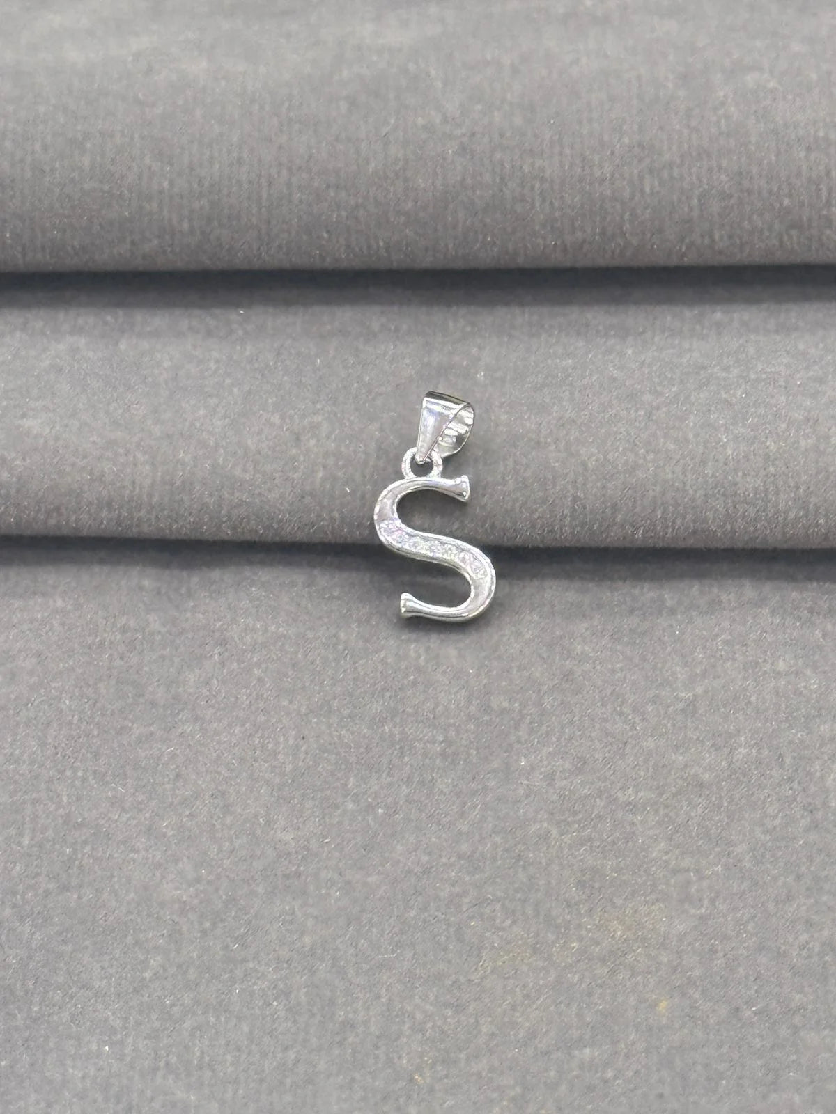 Silver 'S' pendant on a gray fabric background