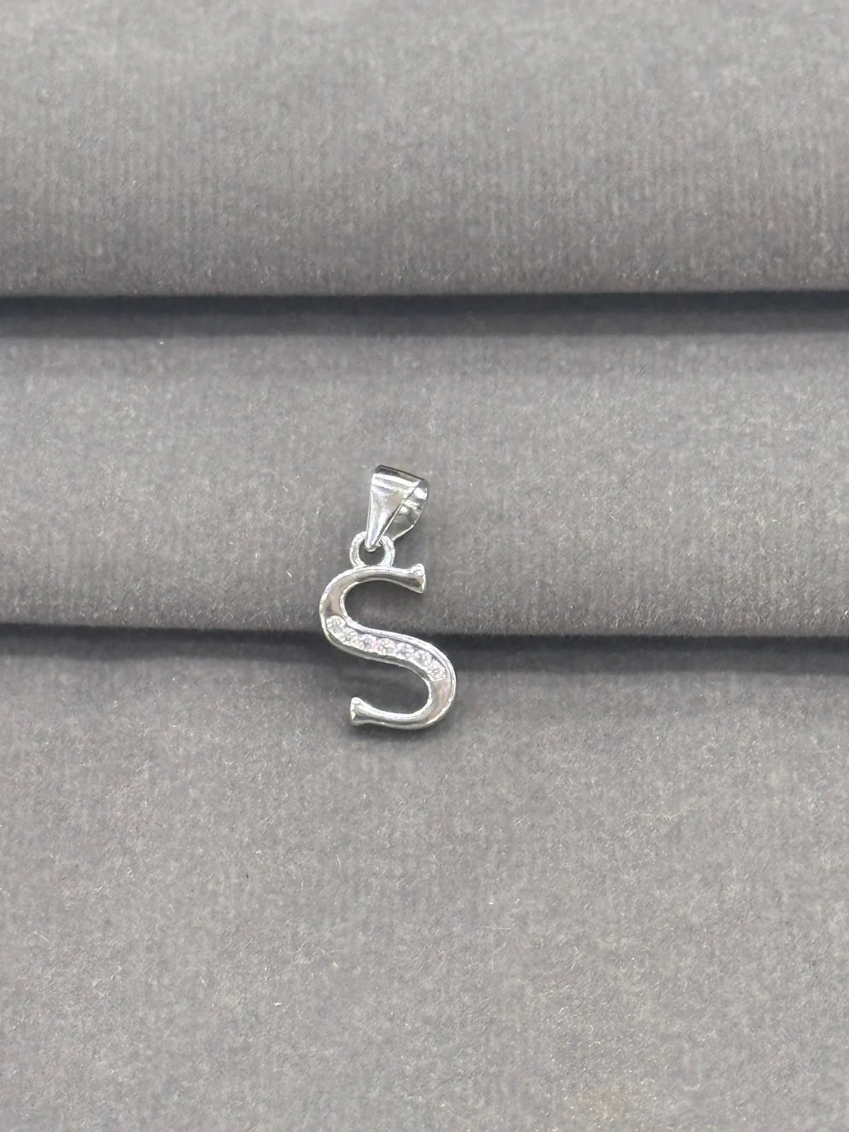 Silver 'S' pendant on a gray fabric background