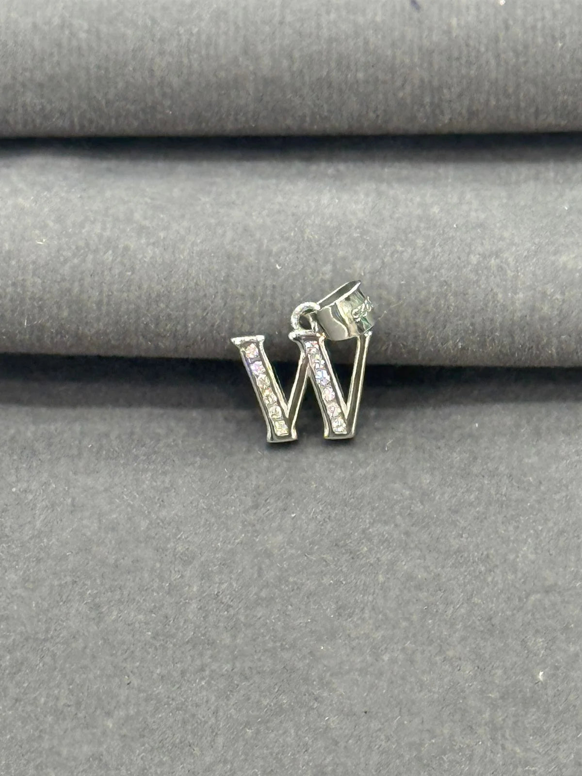 Silver letter 'W' charm with clear stones on a gray fabric background