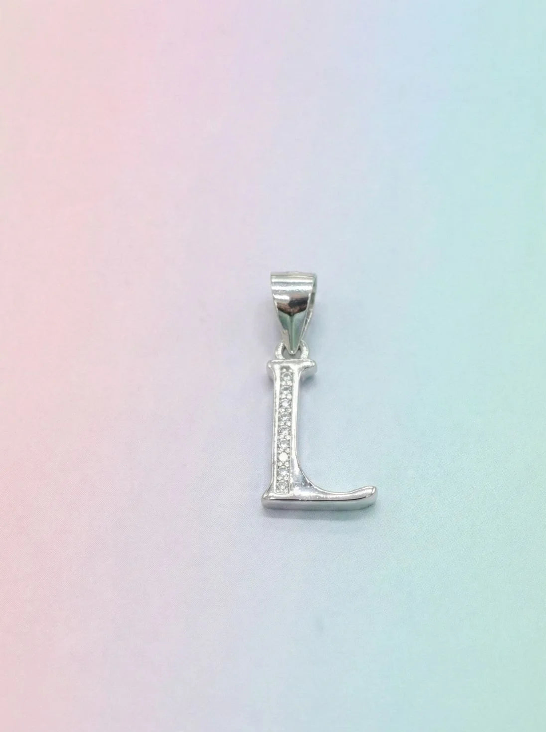 Silver 'L' pendant on a pastel gradient background