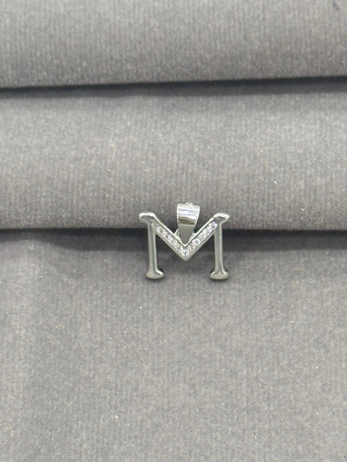 Silver 'M' pendant on a gray fabric background
