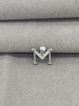 Silver 'M' pendant on a gray fabric background